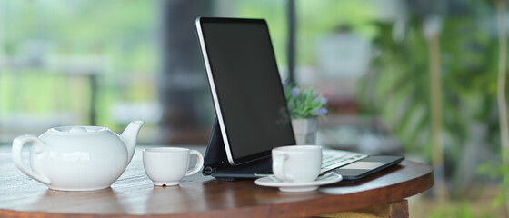 Workspace with mock up blank screen tablet with keyboard with  teapot set on the table
