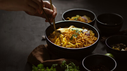 Hand holding silverware to eating Noodles curry soup with Chicken (Khao Soi)