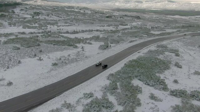 Aerial view pans up to show cars onf snowy mountain road
