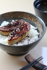 Foie Gras Don - A bowl of steamed rice topped with grilled goose liver topped with roe salmon on wooden table.