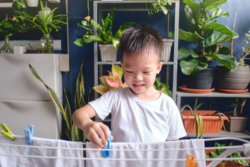 Cute little Asian 4 years old kid having fun hanging clean washed clothes on drying rack for drying at home, Little home helper, chores for kids, Executive Functioning skill development concept