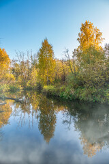 Autumn forest is reflected in the water of river with fog on the water