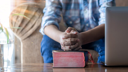 Close up hands of young male praying with bible on wooden table, Online church in home, Home church...