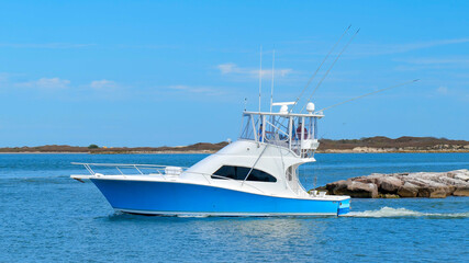 Fototapeta premium Beautiful blue and white fishing yacht boat sails on the calm blue water as it leaves the marina on a sunny day.