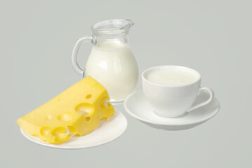 Milk in a jug and in a white cup, a piece of cheese on a saucer.