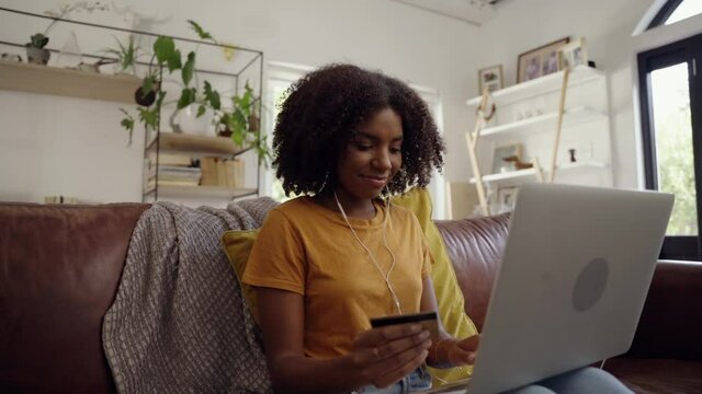A happy young woman sitting at home buying online using laptop and paying with a credit card