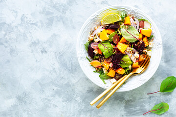 Fresh vegetable salad with beets, arugula, red onions, sorrel, chickpeas, peaches and grapes in a white plate on a white stone background. Top view