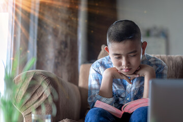 Boy praying on sofa with bible, Home church during quarantine coronavirus Covid-19, Religion concept.