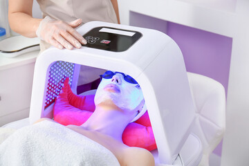 Woman undergoing procedure of facial chromotherapy in beauty salon