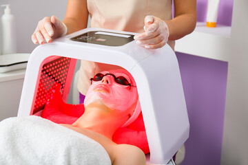 Woman undergoing procedure of facial chromotherapy in beauty salon
