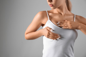 Young woman checking her breast on grey background. Cancer awareness concept