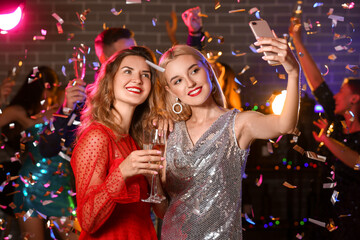 Young women drinking tasty champagne and taking selfie at party in nightclub