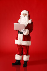Santa Claus with laptop on color background