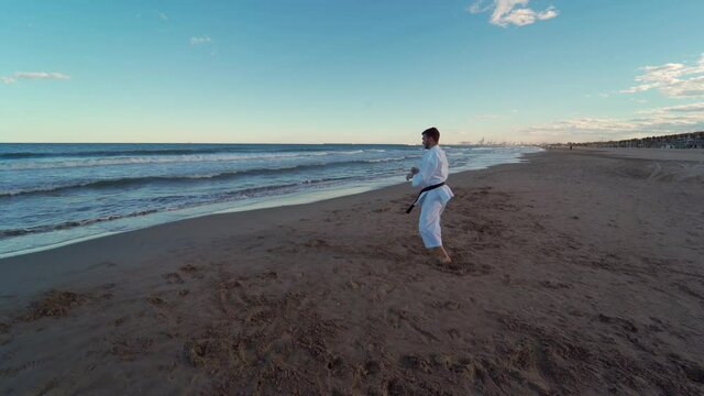 Karate fighter practicing katas on the seashore at sunset. Energetic and powerful karate movements. Karate Shito Ryu. Truck left camera