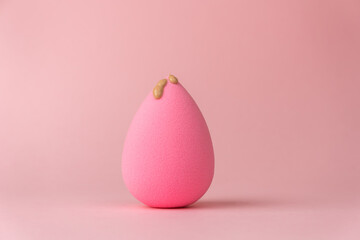 The foundation flows down the sponge for applying makeup in the form of a drop or egg, on a delicate pink background