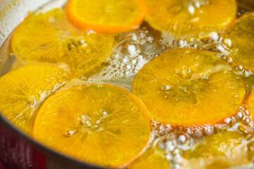 Fototapeta na wymiar Orange slices cooking in bubbling hot syrup in a pot. Making candied orange slice for dessert decoration garnish.