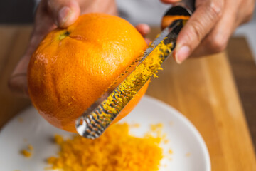 A zester zesting orange skin on a white plate on a wooden tabletop. 