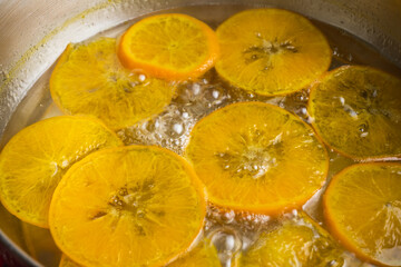 Orange slices cooking in bubbling hot syrup in a pot. Making candied orange slice for dessert decoration garnish.