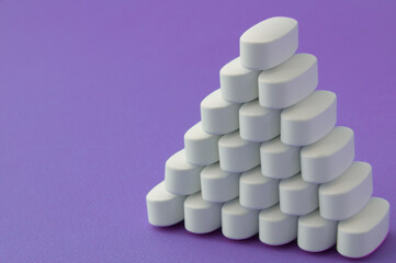 white medication pills tablets on violet purple surface with copy space