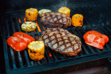 Beef steaks with vegetables on the grill with flames