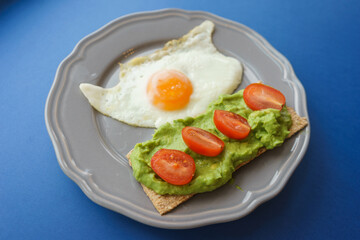 Simple and delicious breakfast: fried eggs on rye bread with guacomole, avocado puree and cherry tomato slices. 