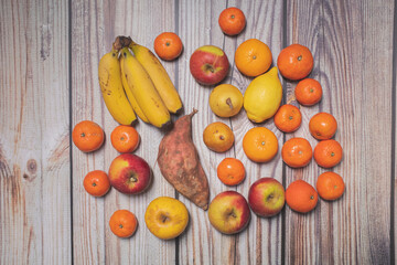 Many different autumn fruits on a wooden board like mandarins, lemos, apples and bananas