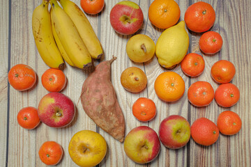 Many different autumn fruits on a wooden board like mandarins, lemos, apples and bananas