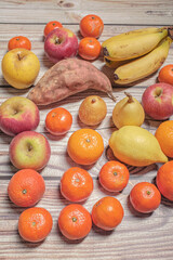 Many different autumn fruits on a wooden board like mandarins, lemos, apples and bananas
