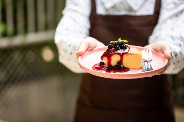 Asian restaurant owner carries a blueberry cake with mints, strawberries jam and forks in pink dish. Sweets that are ready to serve for important customers of all ages. Served with fresh milk