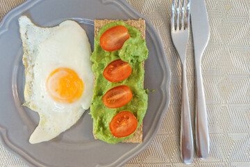 Simple and delicious breakfast: fried eggs on rye bread with guacomole, avocado puree and cherry tomato slices.