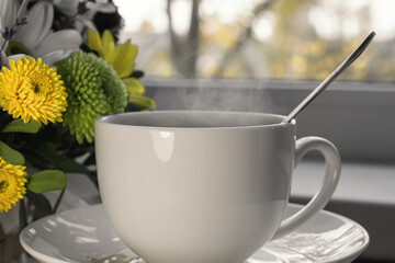near the windowsill with a bouquet of flowers is a white Cup with a hot drink and steam