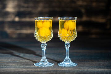 Homemade tincture of yellow cherry plum in a two wine crystal glass on wooden background, Ukraine