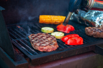 Beef steaks with vegetables on the grill with flames