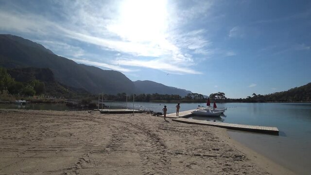 Oludeniz beach, Fethiye, Turkey - 24th of October 2020: 4K Two boys on the lonely beach head to the water cycles
