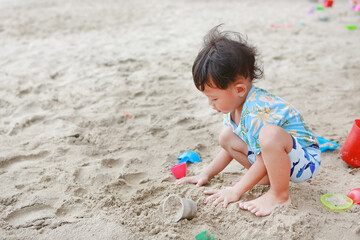Portrait of little asian baby boy play sand with toys on beach