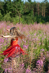 Fototapeta na wymiar cute little blonde girl in an elegant fairy dress whirl in the flowers of fireweed forest. Evening sun rays. Festive mood, birthday during the global pandemic, Coronovirus.