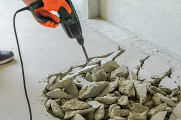 Worker smashes concrete floor with electric hammer drill	
