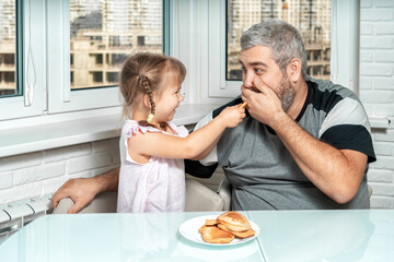a cute little girl laughingly presents cooked pancakes to her gray-haired dad. father jokingly refuses to eat. family values and the concept of joint leisure