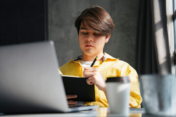Asian man writing idea on a book after found something on internet.