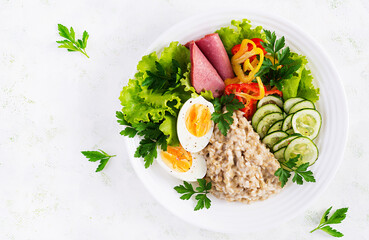 Breakfast oatmeal porridge with boiled egg, ham and vegetables salad. Healthy food. Top view, overhead,  copy space