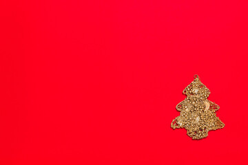 Christmas tree made with golden color material on red background with copy space for text, horizontal. Rich new year toy decorated with glitter bubbles