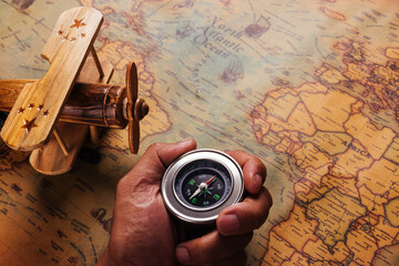 Hand hold old compass discovery and wooden plane on vintage paper antique world map background, Retro style cartography travel geography navigation, Columbus Day concept