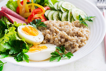 Breakfast oatmeal porridge with boiled egg, ham and vegetables salad. Healthy food.