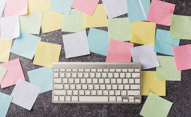Above many blank paper stick note list with the modern computer keyboard on concrete background,...