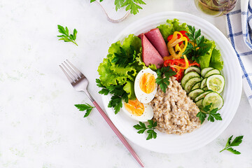 Breakfast oatmeal porridge with boiled egg, ham and vegetables salad. Healthy food. Top view, overhead,  copy space