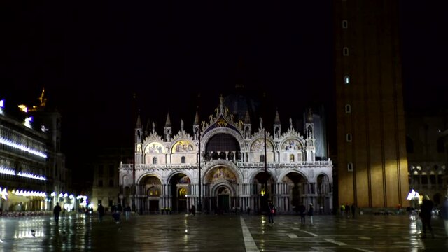 San Marco Basilica Church and Piazza at Night, Venice, Italy. Landmark Exterior and Few People on Square, Static View - empty due to Covid Corona Virus Pandemic, with wet reflective cement after rain