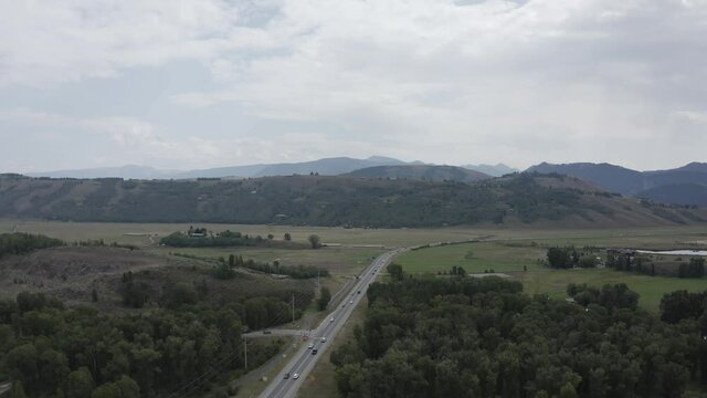 Aerial View of Highway Traffic Outside Jackson, Wyoming USA on Cloudy Summer Day looking Towards the Teton Mountain Range Green and Brown Landscape. Few Cars Due To Covid 19 Corona Virus Pandemic