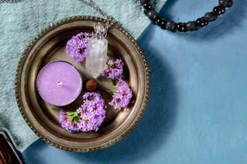 Aromatherapy banner with a place for text. Aromatic candle, vial for perfume, vervain flowers and a lava bracelet, shot from above on a blue background