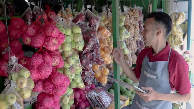 a male shop owner holding a digital tablet while observing fresh fruit in a fruit shop
