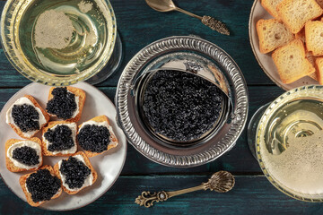 Black caviar with champagne in vintage coupe glasses, with toasts, a flat lay, top shot on a dark...